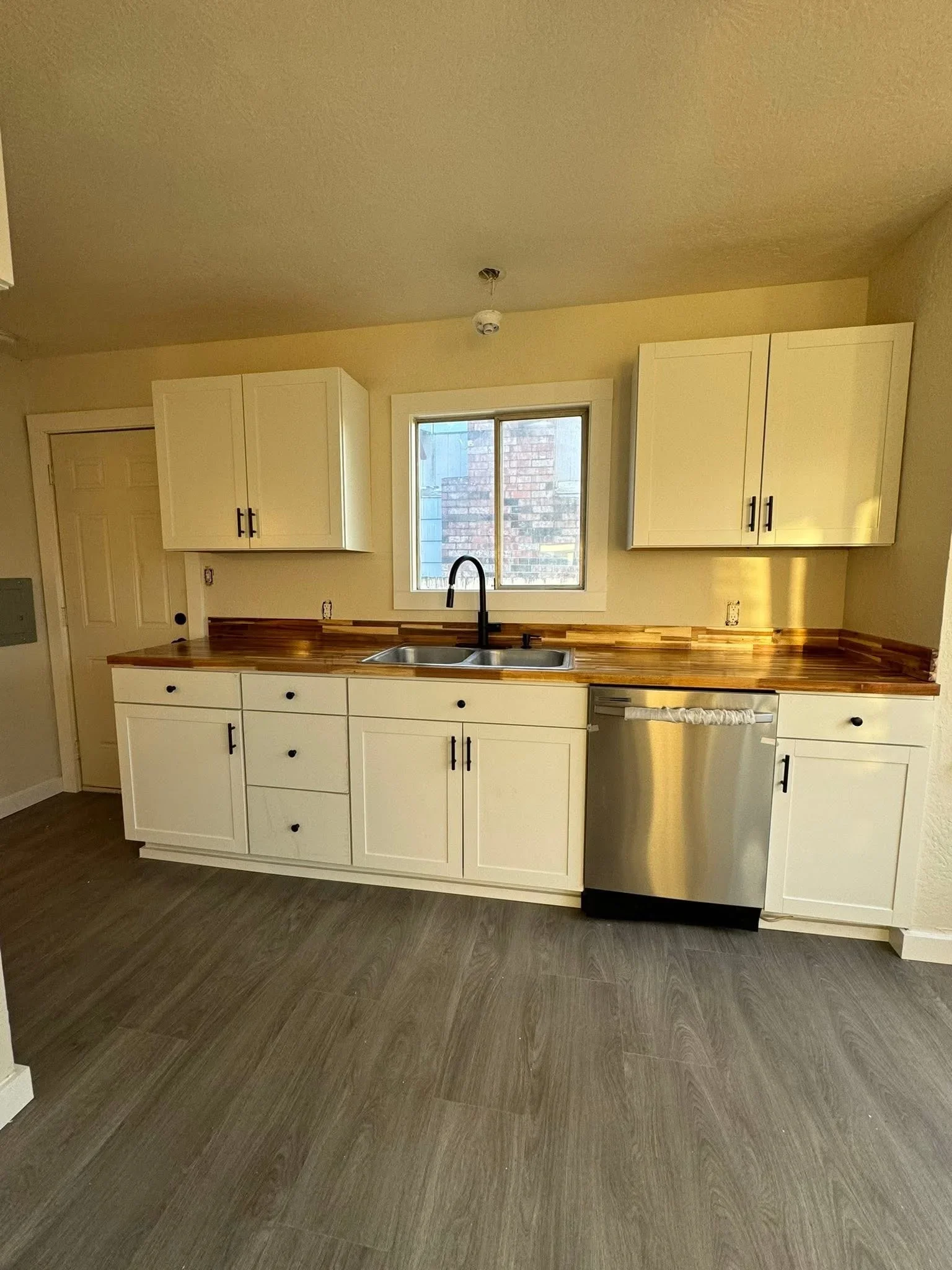 Cream cabinetry with wood countertops, stainless steel dishwasher and sink, vinyl plank flooring