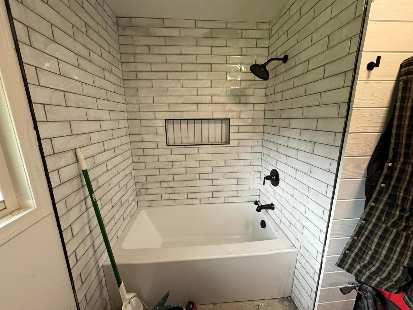 White subway tile shower surround with black grout, white tub, and black fixtures