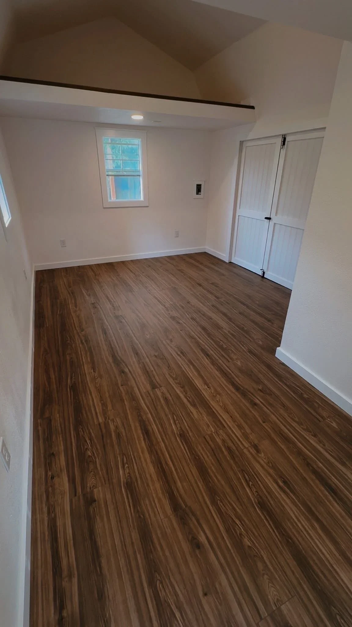 Spacious room with dark wood-grain vinyl plank flooring, white walls, vaulted ceiling, recessed lighting, and white interior doors