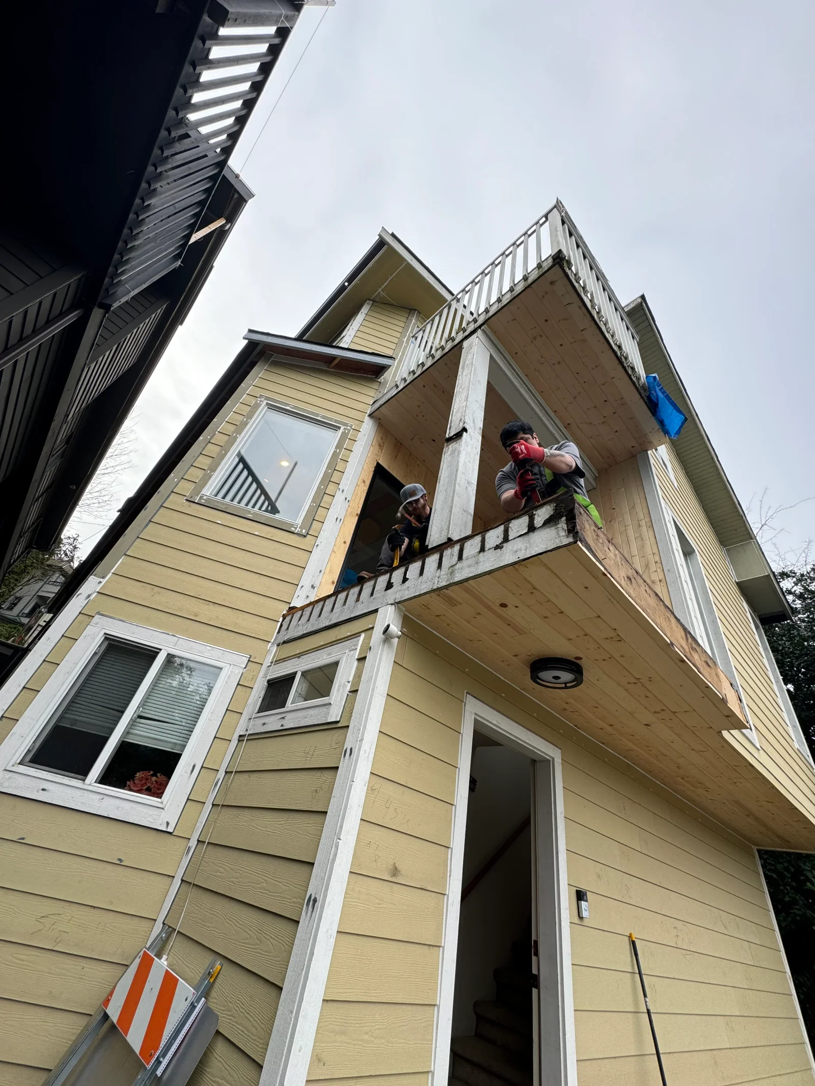 Workers installing white vinyl railings and composite decking on multi-story residential deck structure