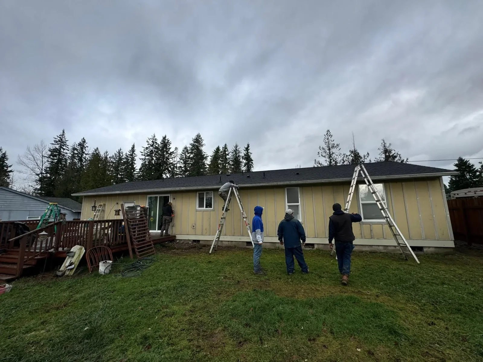 Home exterior with new cream siding, dark gray roof, and aluminum ladders during installation