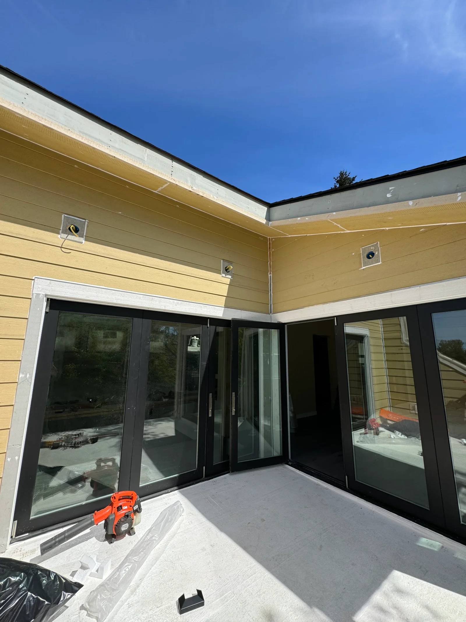 Black bifold patio doors with white trim installed on yellow siding exterior