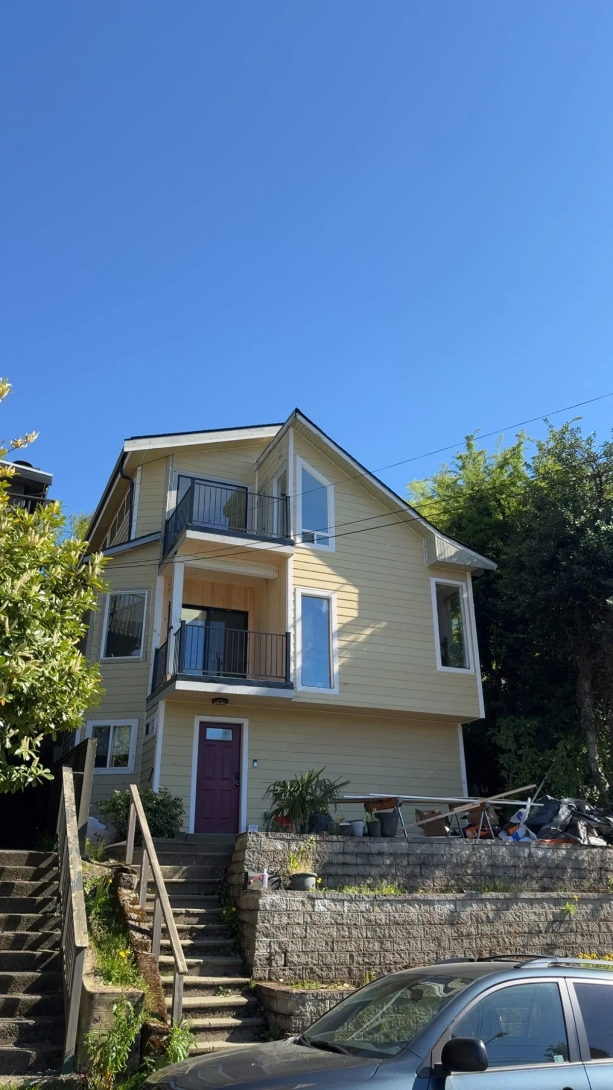 Three-story home with new tan siding, metal deck railings, replacement windows, and stone retaining wall