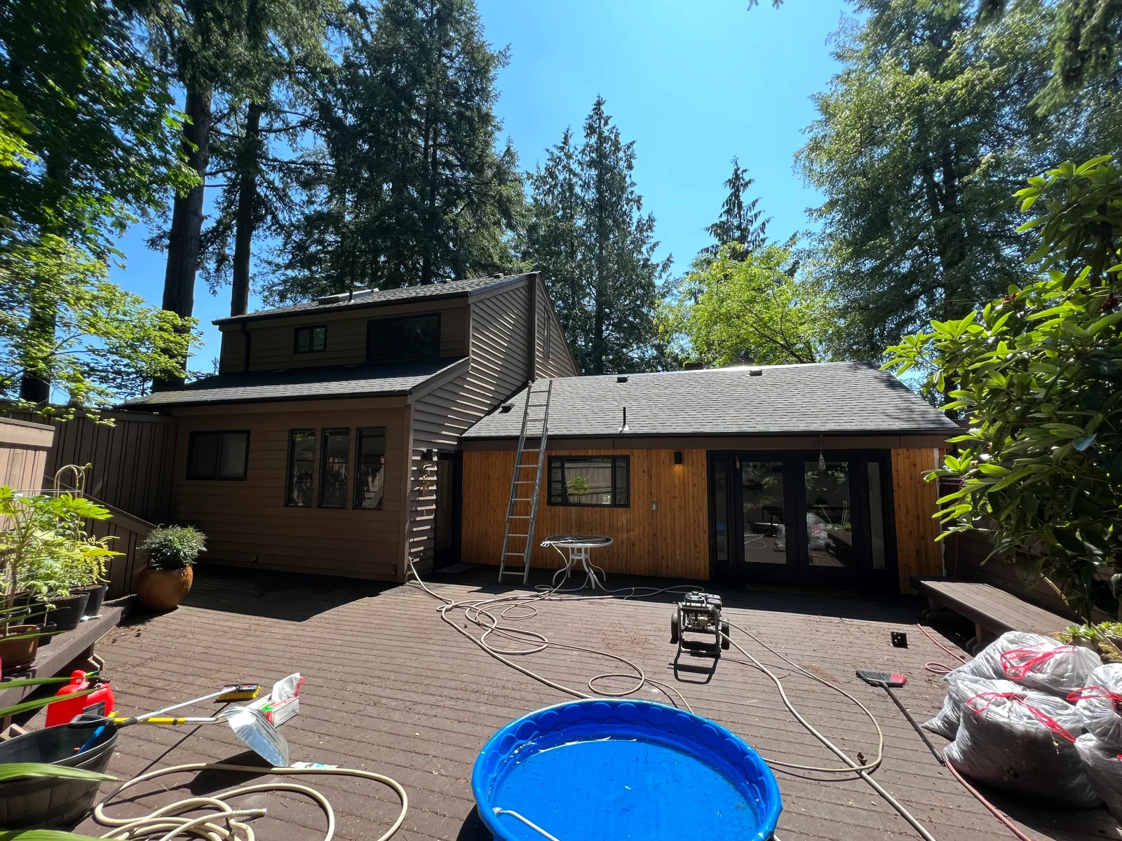 Modern home addition with wood and metal siding, composite deck, and black-framed windows surrounded by tall trees