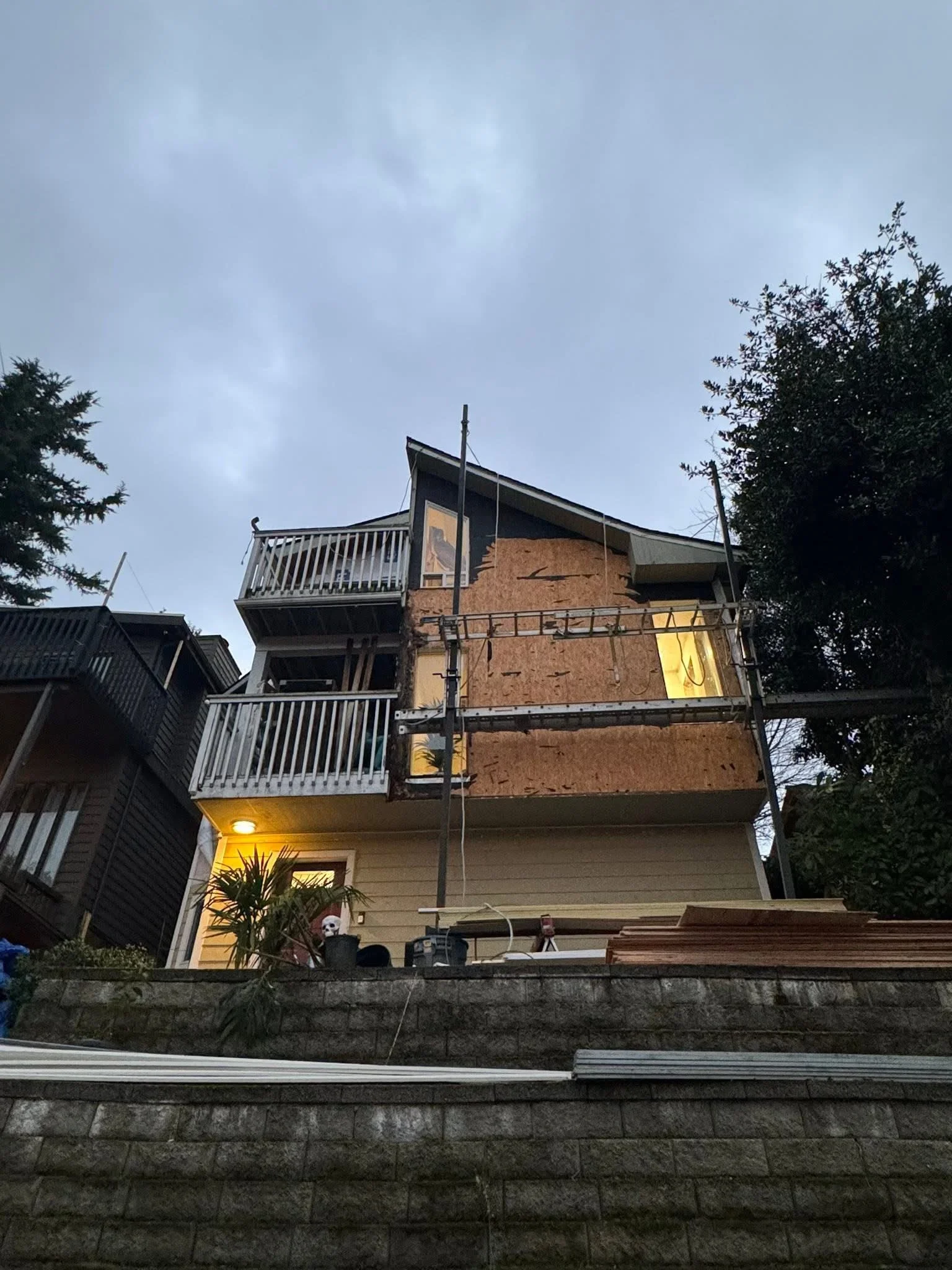 Multi-story home exterior with metal scaffolding, plywood sheathing, and metal deck railings during renovation