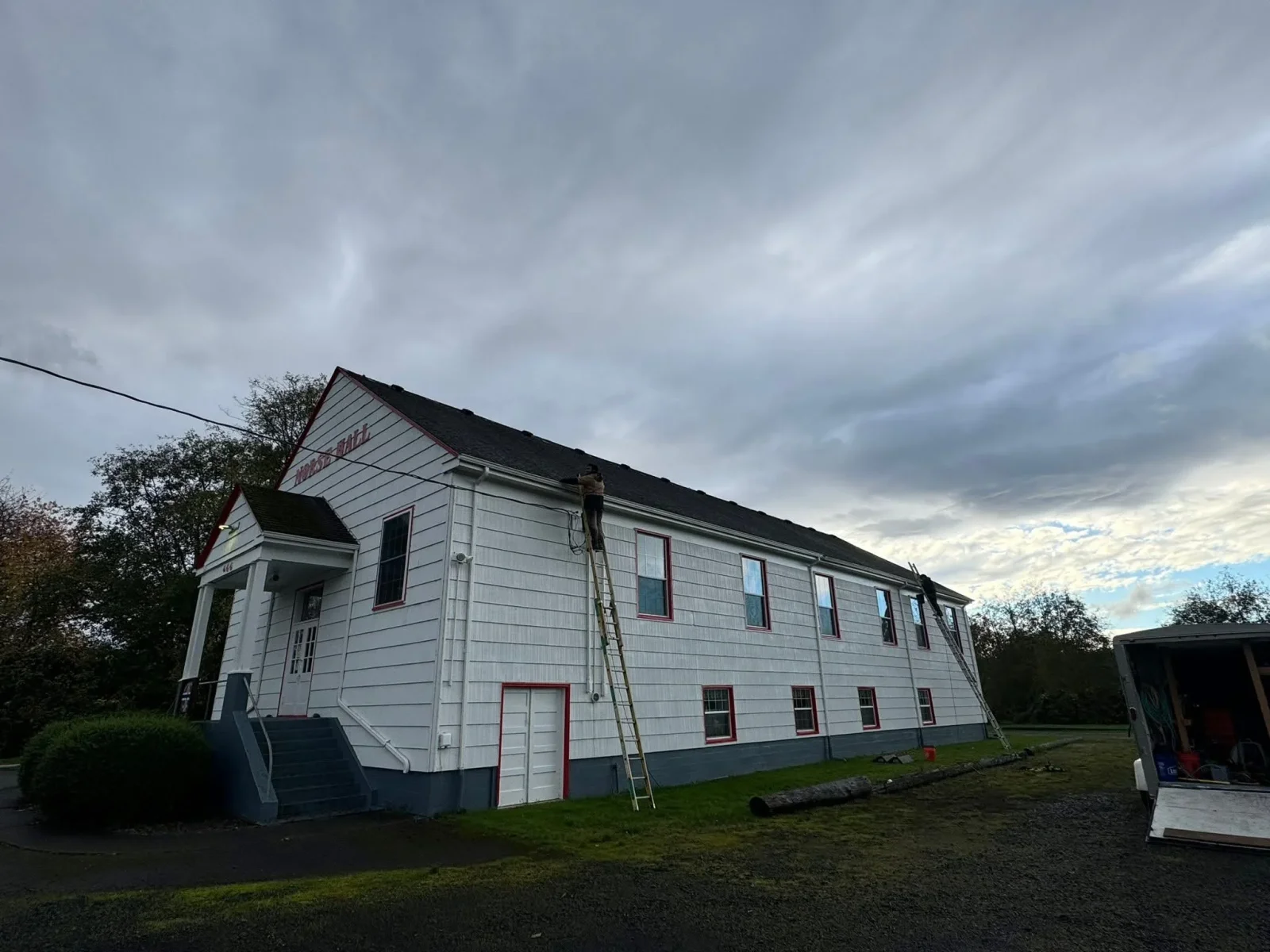 Two-story white lap siding building with black roof, red trim, and new windows during restoration