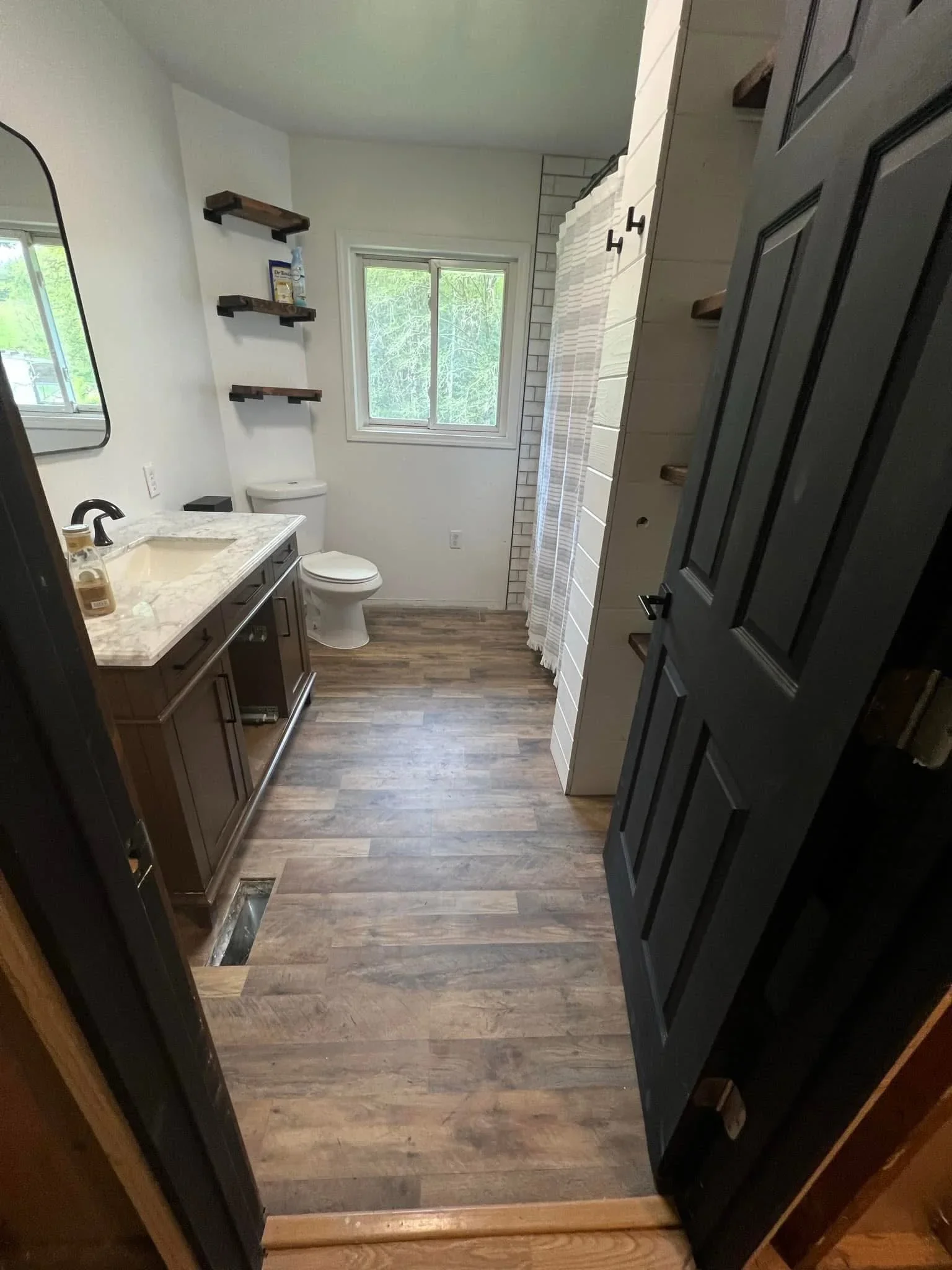 Renovated bathroom with marble vanity, vinyl plank flooring, subway tile shower, and floating shelves