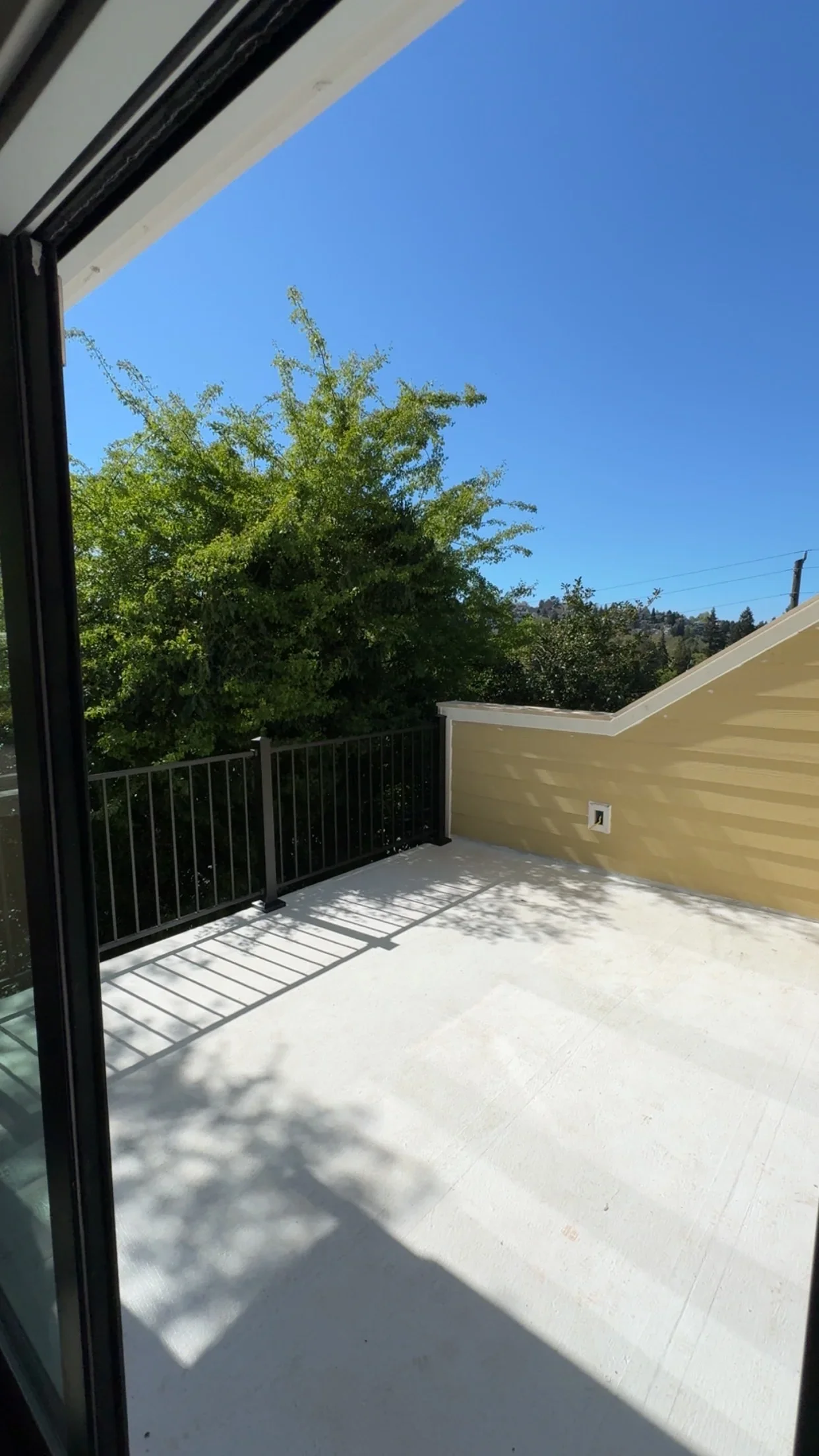Concrete deck with black metal railing and yellow siding, overlooking trees