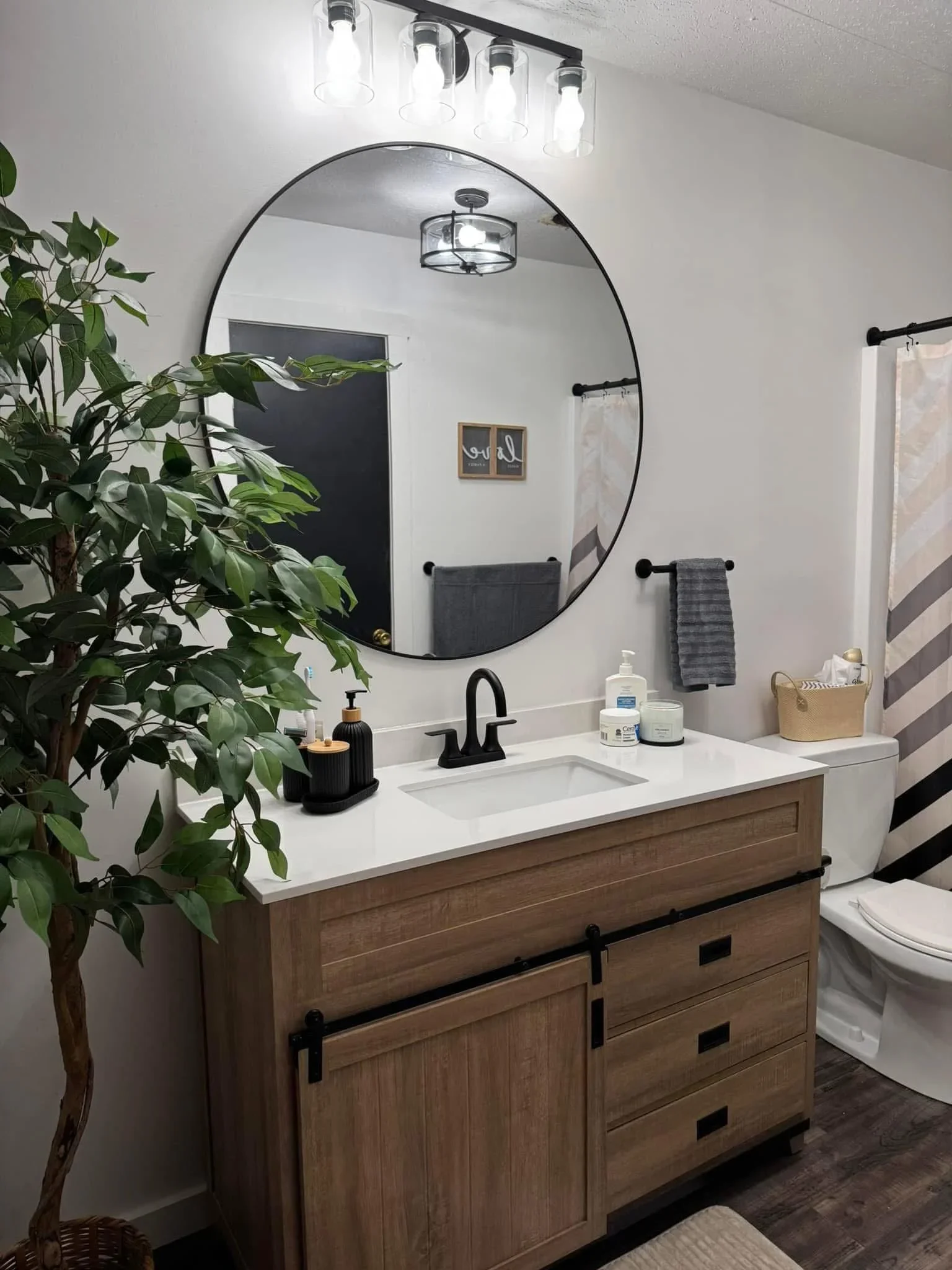 Wood vanity with white quartz countertop, black-framed mirror, and modern lighting fixtures