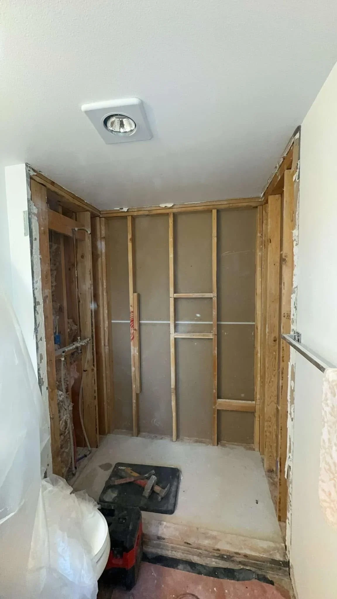 Bathroom interior framing with wood studs, drywall panels, and recessed ceiling light