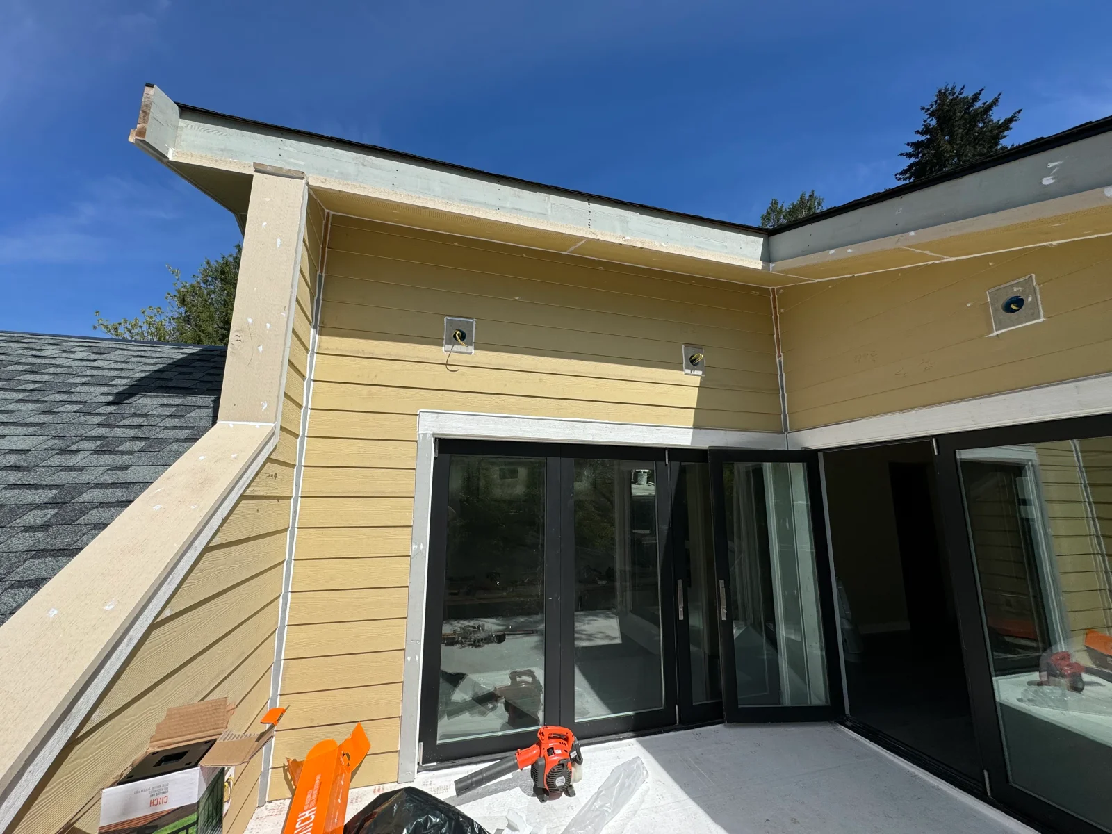 Tan composite siding addition with black multi-panel sliding glass doors and white soffit trim